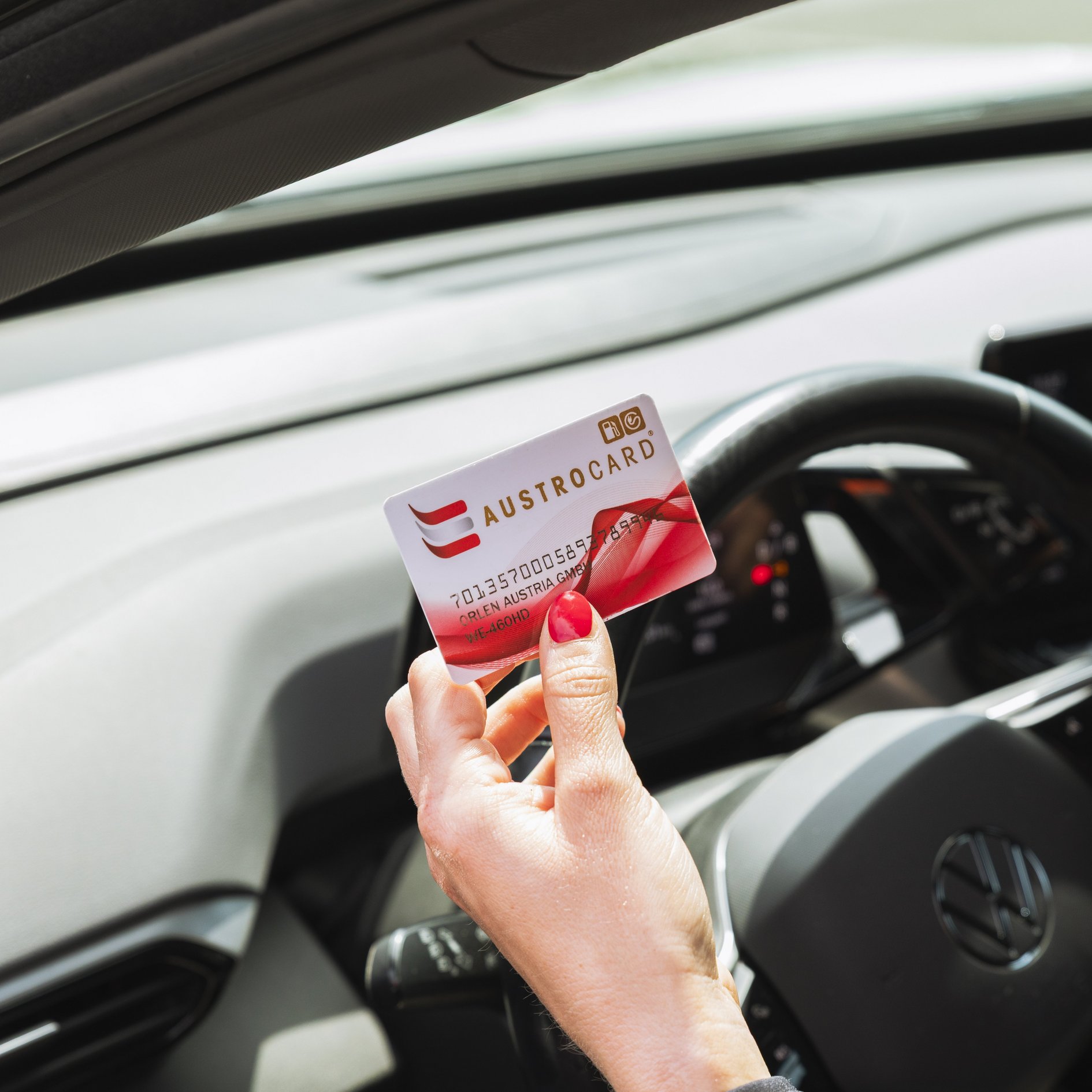 Hand hält eine AUSTROCARD im Innenraum eines Autos vor dem Lenkrad.
