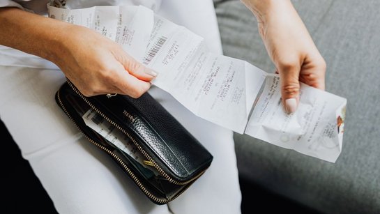 Person holding several receipts above an open wallet.